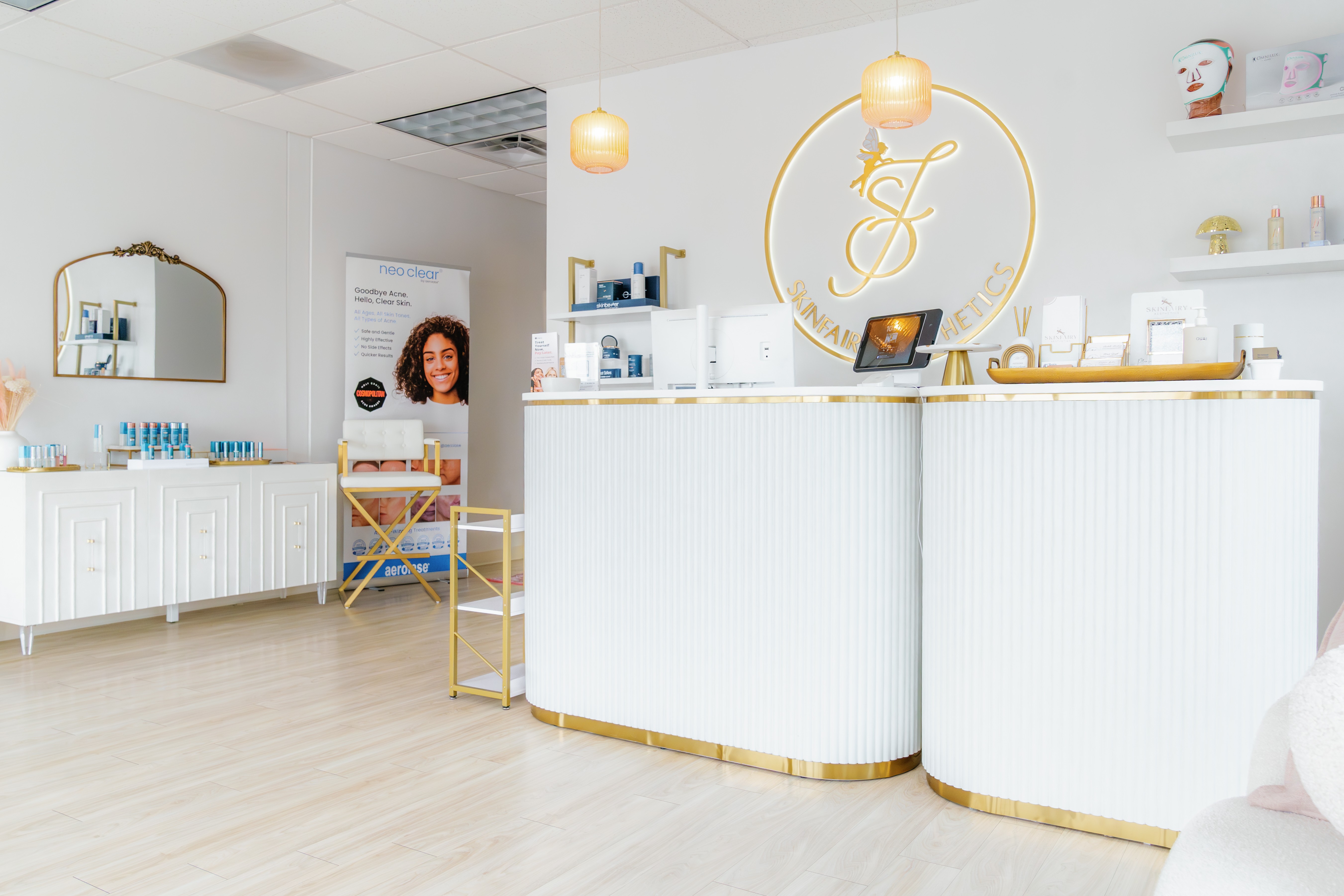 Reception area with white curved counter, gold accents, shelves, and a large circular logo on the wall, bright lighting.