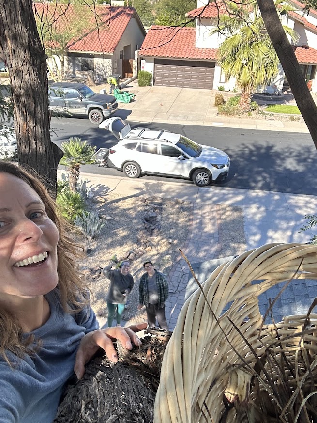 Person smiling outdoors with a view of a street, parked cars, and two people standing on the sidewalk.