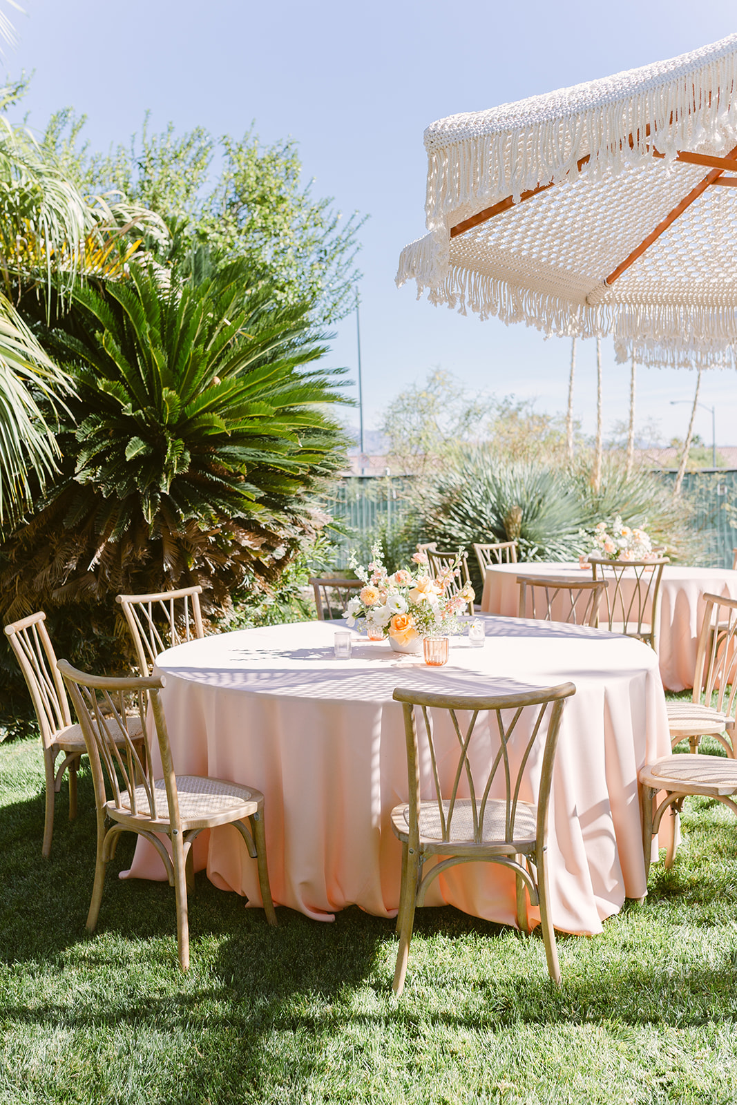Outdoor garden setting with round table, chairs, large umbrella, and lush greenery under a clear sky.