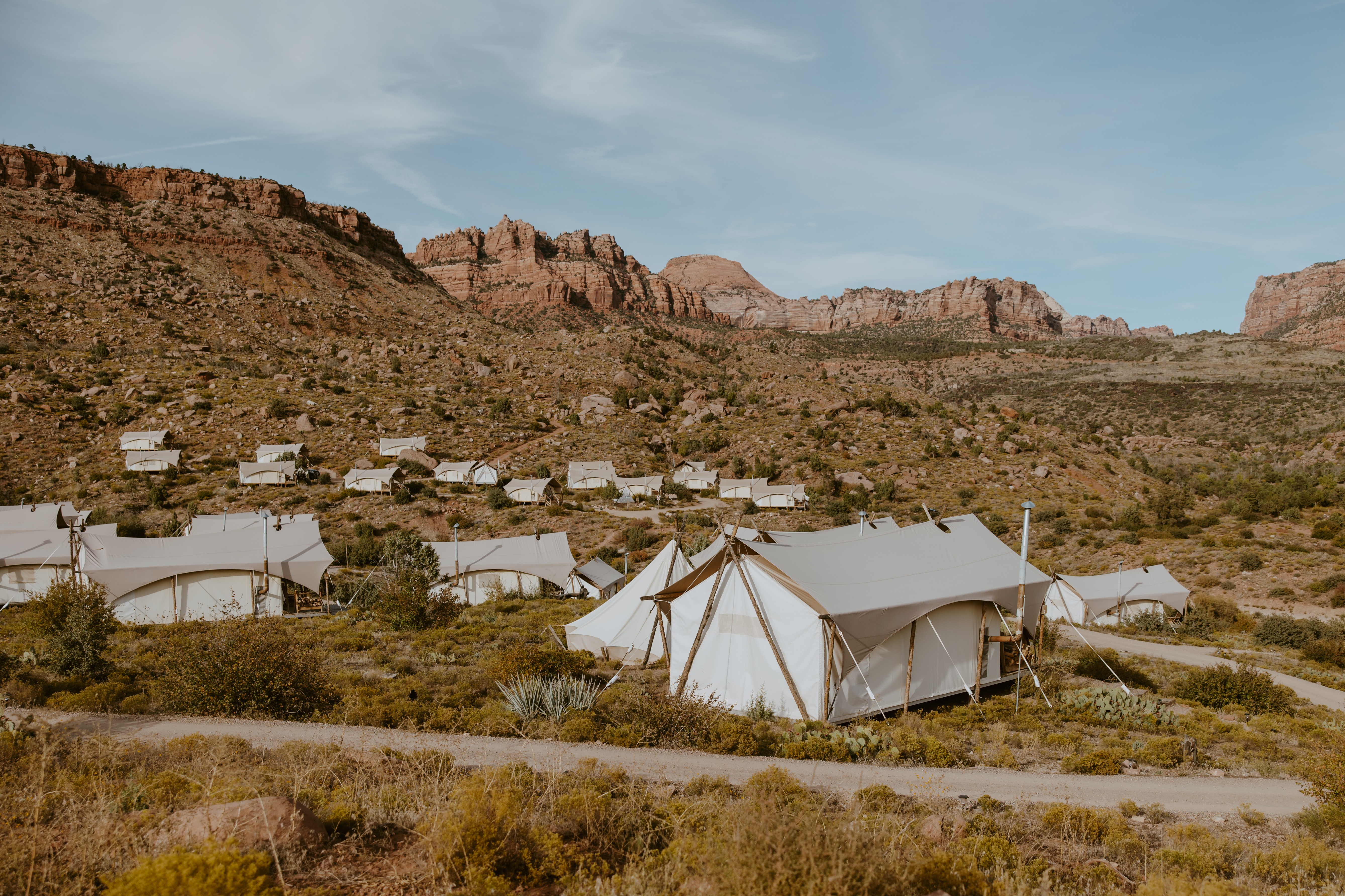 Tents set up on a desert landscape with rocky hills in the background under a blue sky.