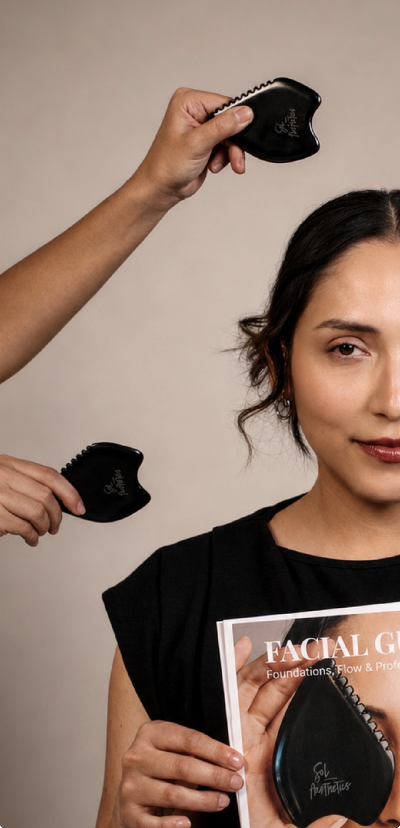 Person holding a facial device near face, another person holding a similar device, woman holding a magazine, neutral background.