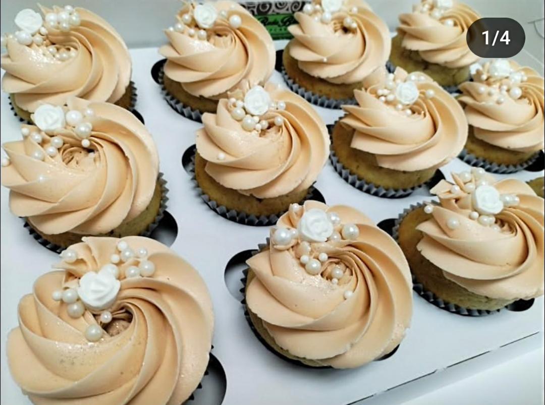 Cupcakes with beige frosting and pearl decorations arranged on a white surface.