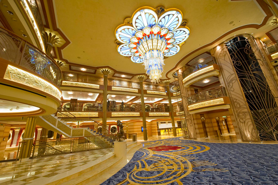 Luxurious hotel lobby with a large stained glass chandelier, ornate decor, and a patterned carpet, viewed from the entrance.