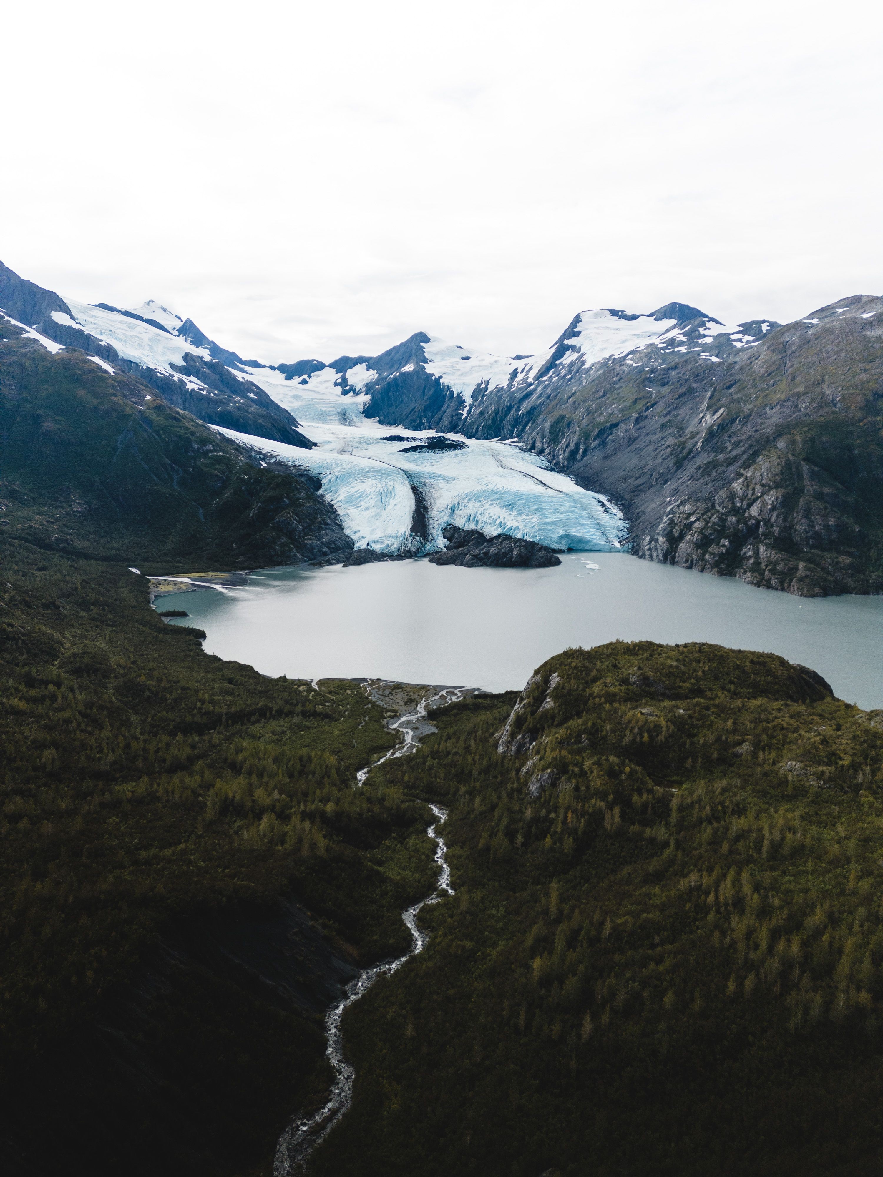 Mountain landscape with glacier, lake, and river, under cloudy sky.
