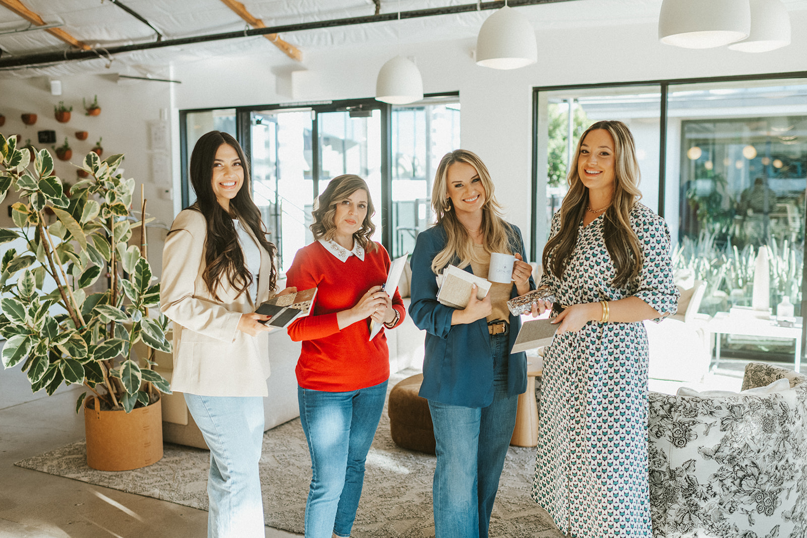 Four women standing together in a bright, modern room, smiling and holding books or notebooks.