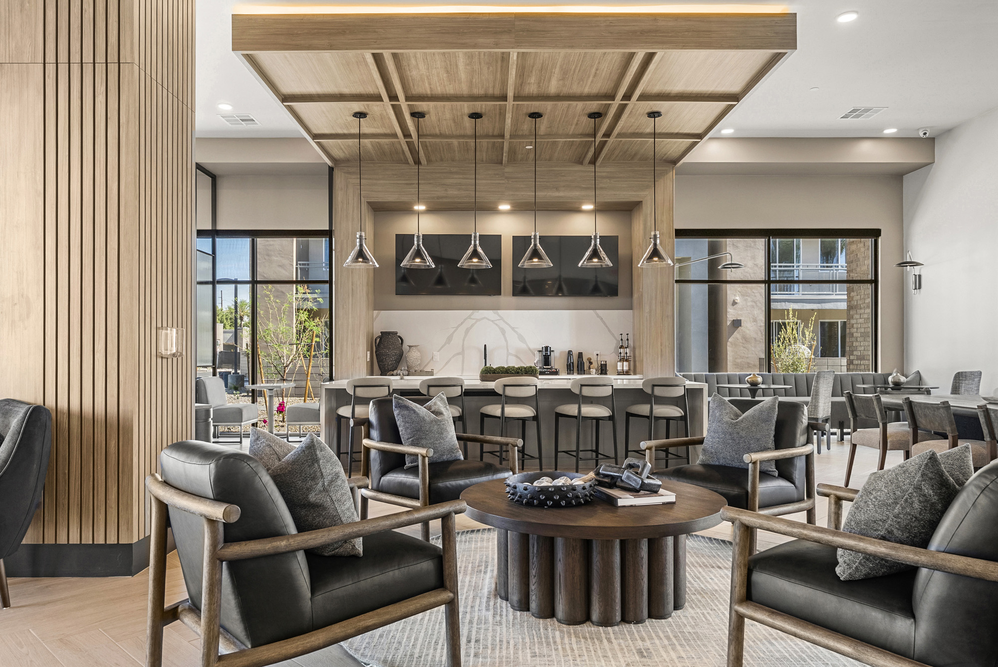 Modern lounge area with black armchairs, a round coffee table, and a view of a kitchen with bar stools and pendant lights.