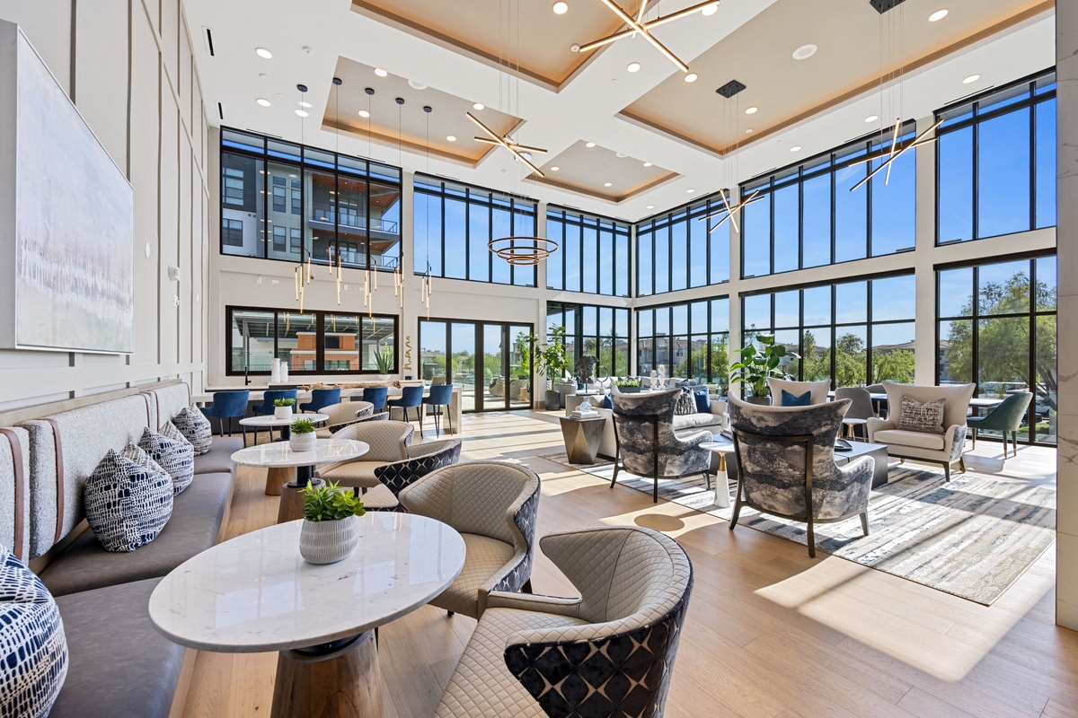 Spacious lounge with large windows, modern furniture, and a high ceiling, filled with natural light and outdoor views.