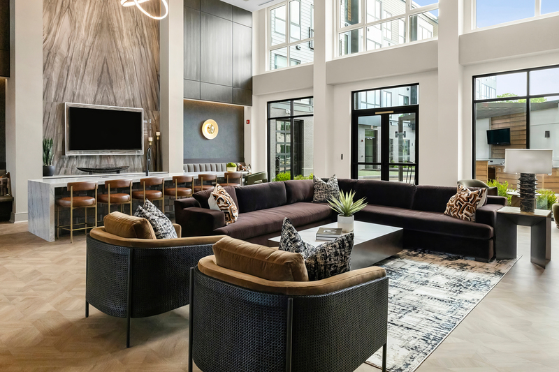 Modern living room with large windows, black sectional sofa, armchairs, and a TV on the wall.